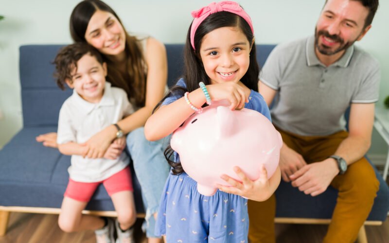 portrait cute little girl putting money pink piggy bank save new toy her her small brother